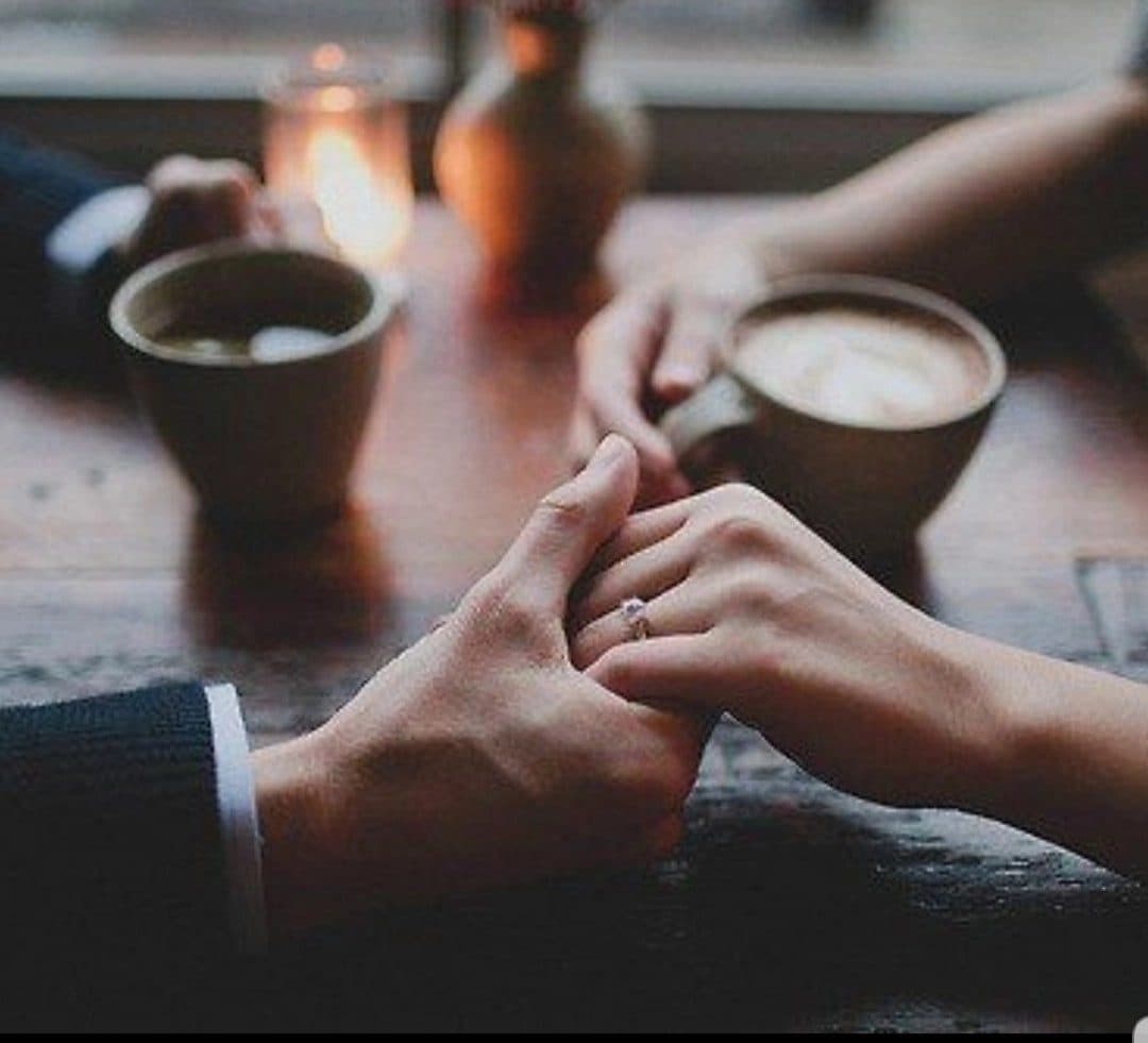 Two hands intertwined across a cafe table beside coffee cups