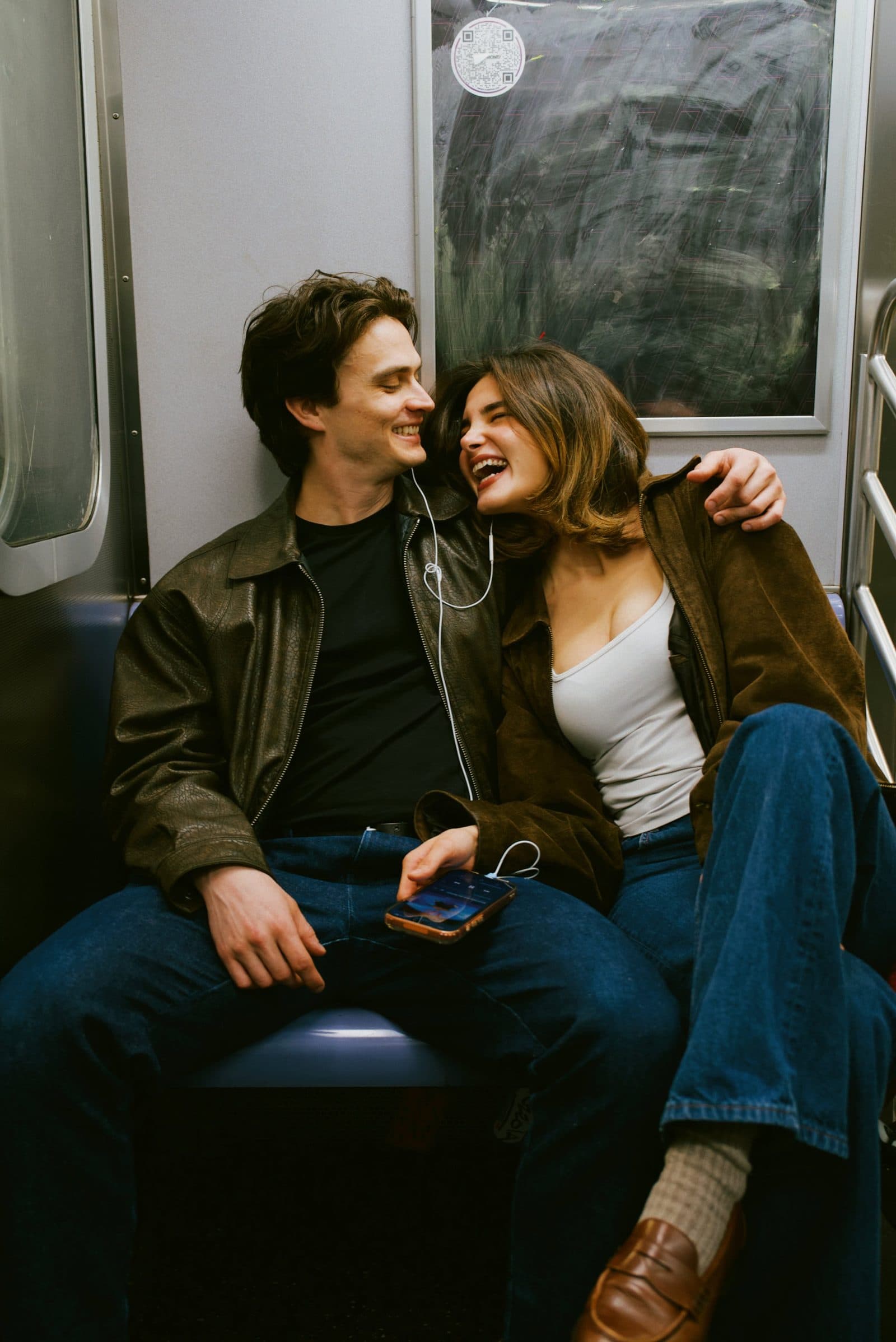 A new couple laughing on the subway sharing earbuds