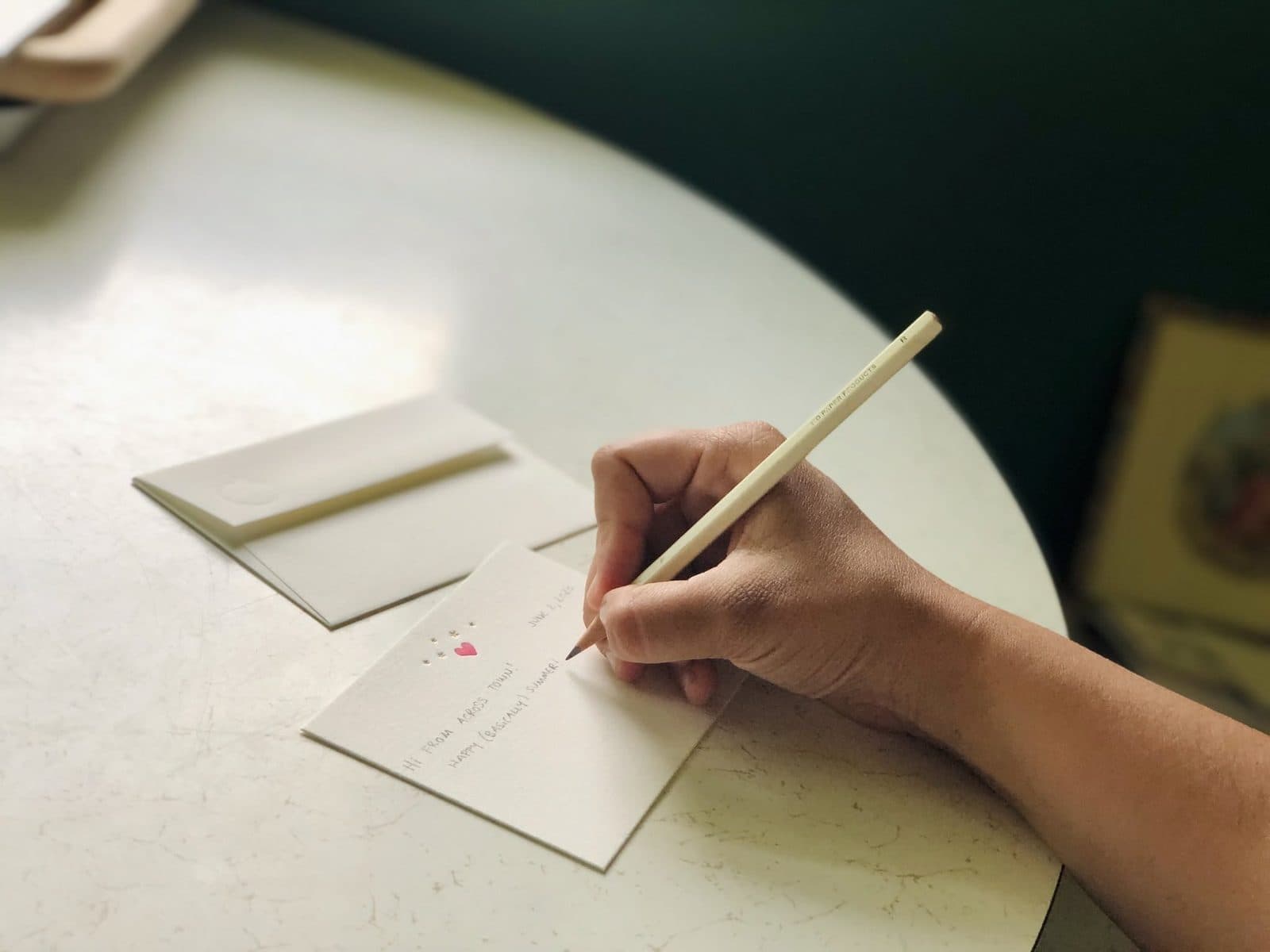A hand writing a small love note card beside its envelope