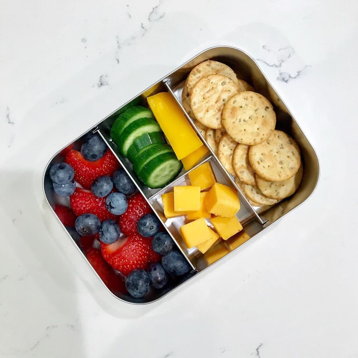 A homemade bento-style kids lunch with crackers, cheese, and fruit