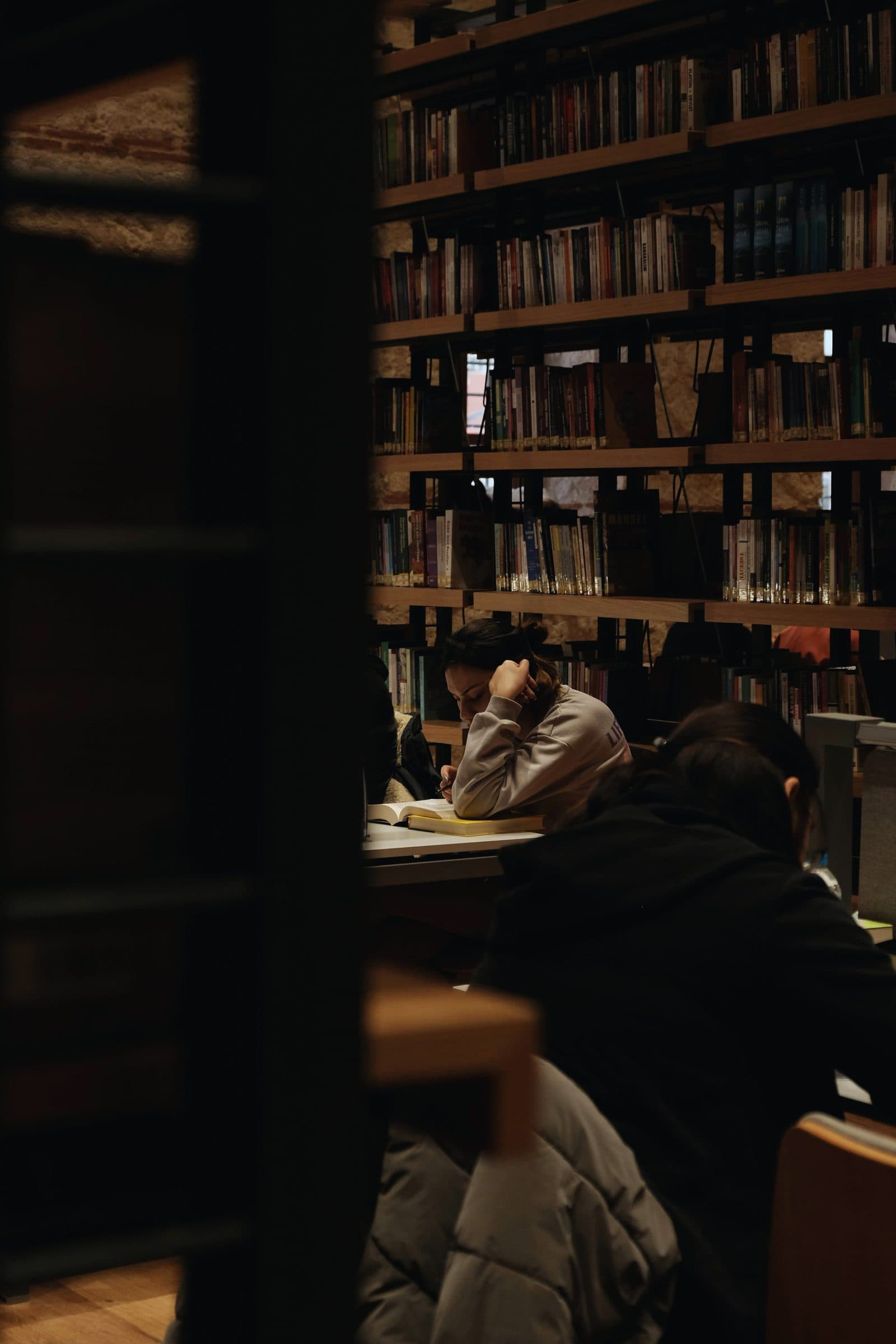 A student studying alone at a library table with a wall of books behind